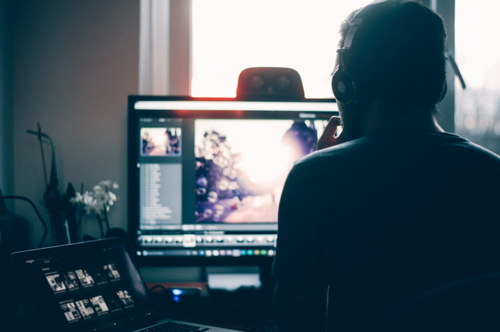 Person arbeitet am Laptop und Monitor in dunkler, fokussierter Atmosphäre
